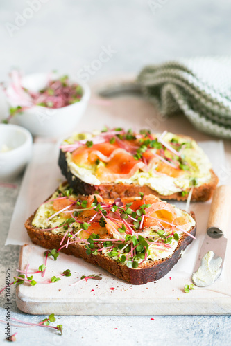 Healthy eating. Toast with avocado cream and smoked salmon on the white wooden board. Smoked salmon, cream cheese and pesto toast sandwiches with radish microgreens sprouts.