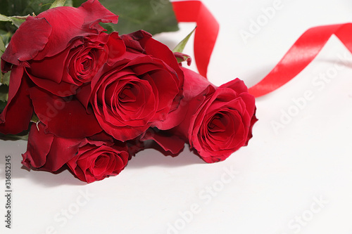 Fototapeta Naklejka Na Ścianę i Meble -  Greeting card for Valentine's Day or Women's Day. Red roses with a ribbon on a white background. Festive background February 14, place for text, banner .Happy birthday, wedding.