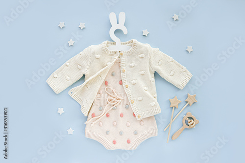 Pastel knitted romper with dots and jumper on cute hanger with bunny ears for baby. Fashion newborn clothes on pink background. Flat lay, top view photo