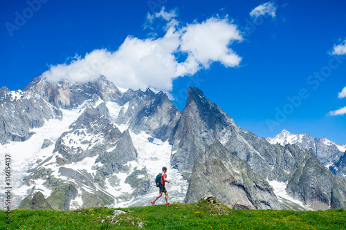 Canvas Print A trail runner running below the high snowy mountains along a grassy ridge in the Alps along the Tour du Mont Blanc route