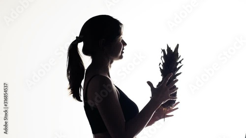 silhouette of a young sports woman throwing fruit of pineapple from hand to nhand, girl supports a healthy lifestyle and nutrition on a white isolated background photo