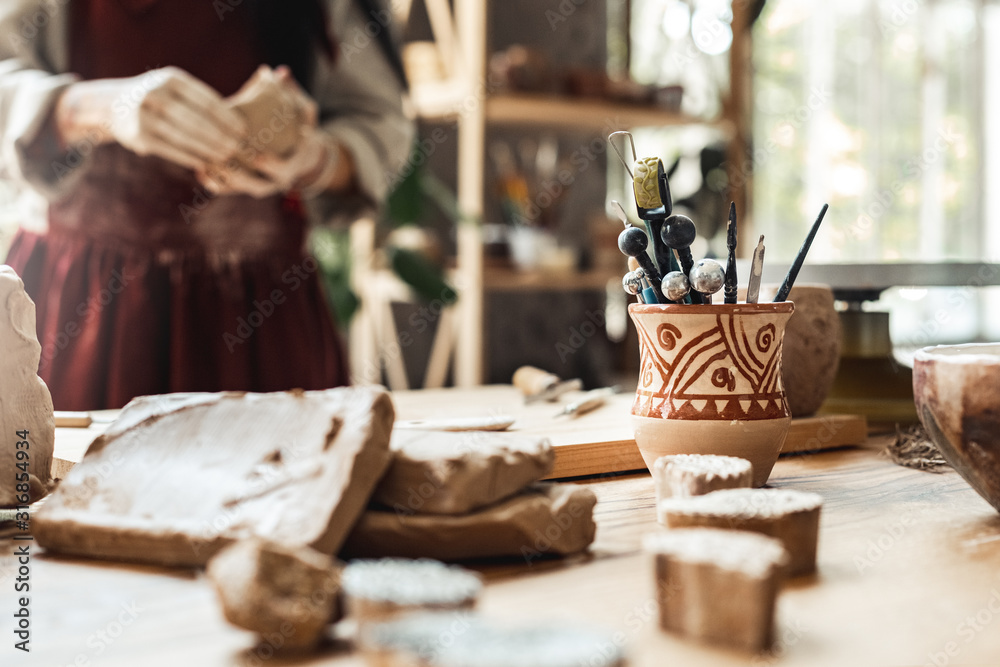 Craftsperson Concept. Young woman making pottery indoors tabl with creations material and tools close-up blurred background - obrazy, fototapety, plakaty 