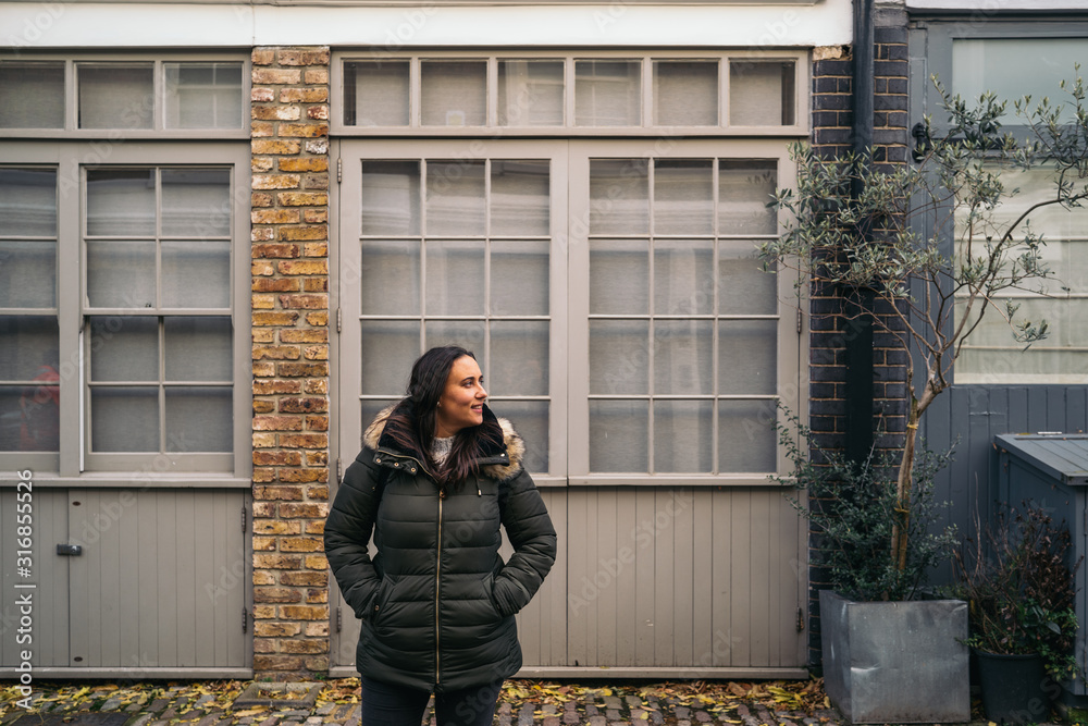 Fototapeta premium Young woman leaving her house and using her smart mobile with colorful houses on Portobello Street in the Notting Hill neighborhood