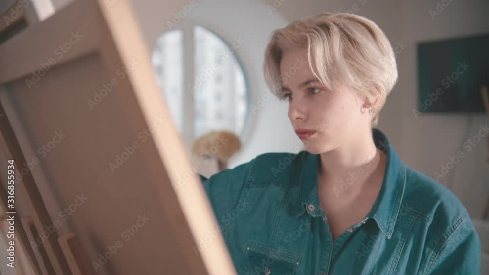A young blonde woman artist draws a painting in the art studio A young blonde woman artist draws a painting in the art studio