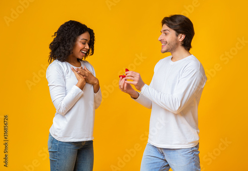 Romantic guy proposing to his surprised girlfriend, giving ring