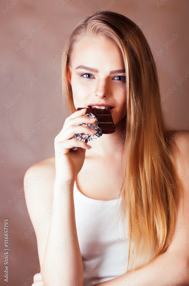 young cute blond girl eating chocolate and smiling on brown background, lifestyle people concept young cute blond girl eating chocolate and smiling on brown background, lifestyle people concept