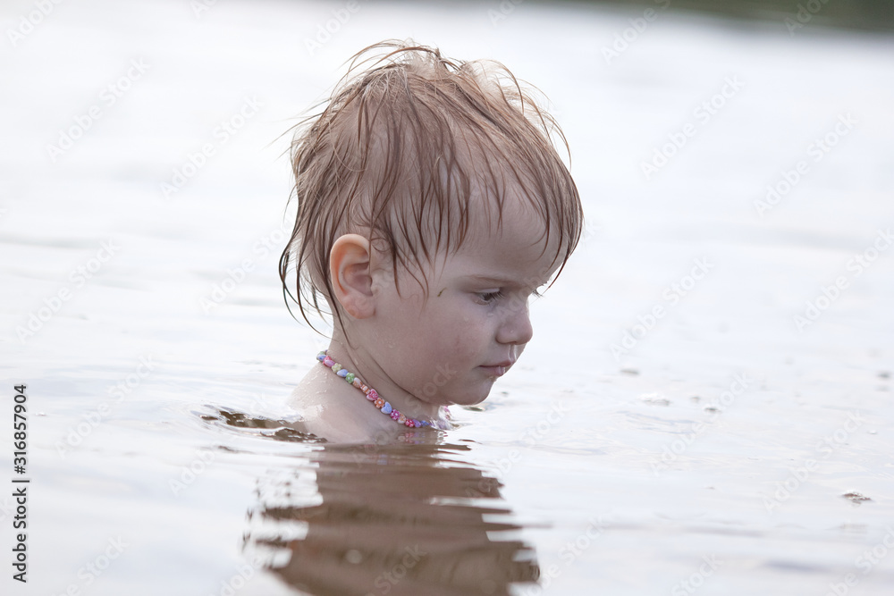 Fototapeta premium little independent girl sitting in the water on the lake