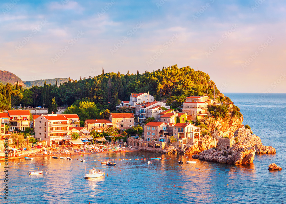 Picturesque summer view of Adriatic sea coast in Budva Riviera. Przno village with buildings on the rock at sunset warm sunlight, Montenegro