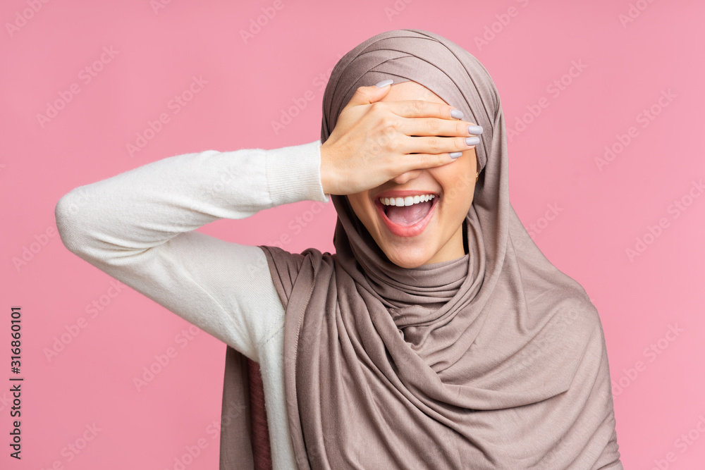 Happy Islamic Woman Covering Eyes With Hand And Smiling, Pink Background Happy Islamic Woman Covering Eyes With Hand And Smiling, Pink Background