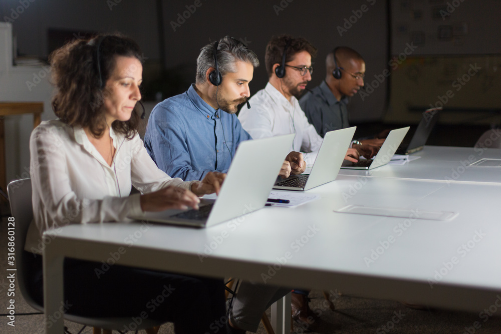 Serious call center operators typing on laptops. Confident client support team at workplace. Call center concept Serious call center operators typing on laptops. Confident client support team at workplace. Call center concept