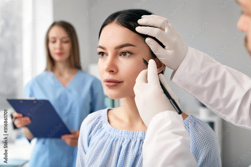 Plastic surgeon applying marks on patient's face in clinic Plastic surgeon applying marks on patient's face in clinic