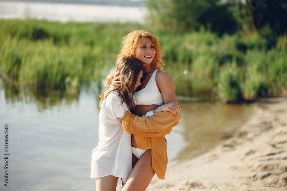 Family near a lake. Beautiful mother with cute daughter. Girls in a stylish swimsuits Family near a lake. Beautiful mother with cute daughter. Girls in a stylish swimsuits