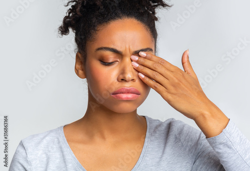Sad black girl touching her eye, suffering from conjuctivitis