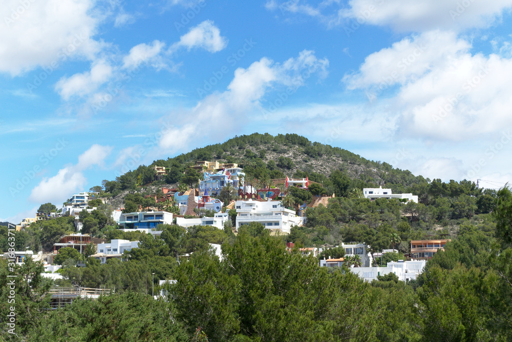 Cloudy rocky mountain with grass, trees and houses. Ibiza island, Spain