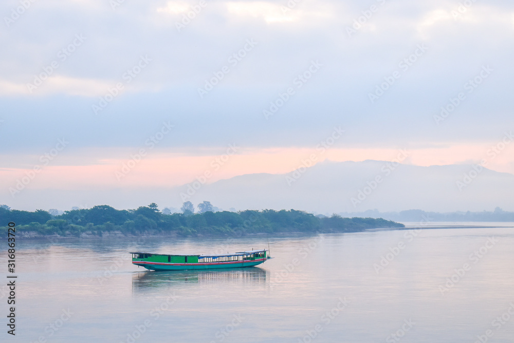 Landscape  of green boat floating on the Mekong in the morning. The sky behind is cloudy and very foggy but cat see shadow of the mountains.