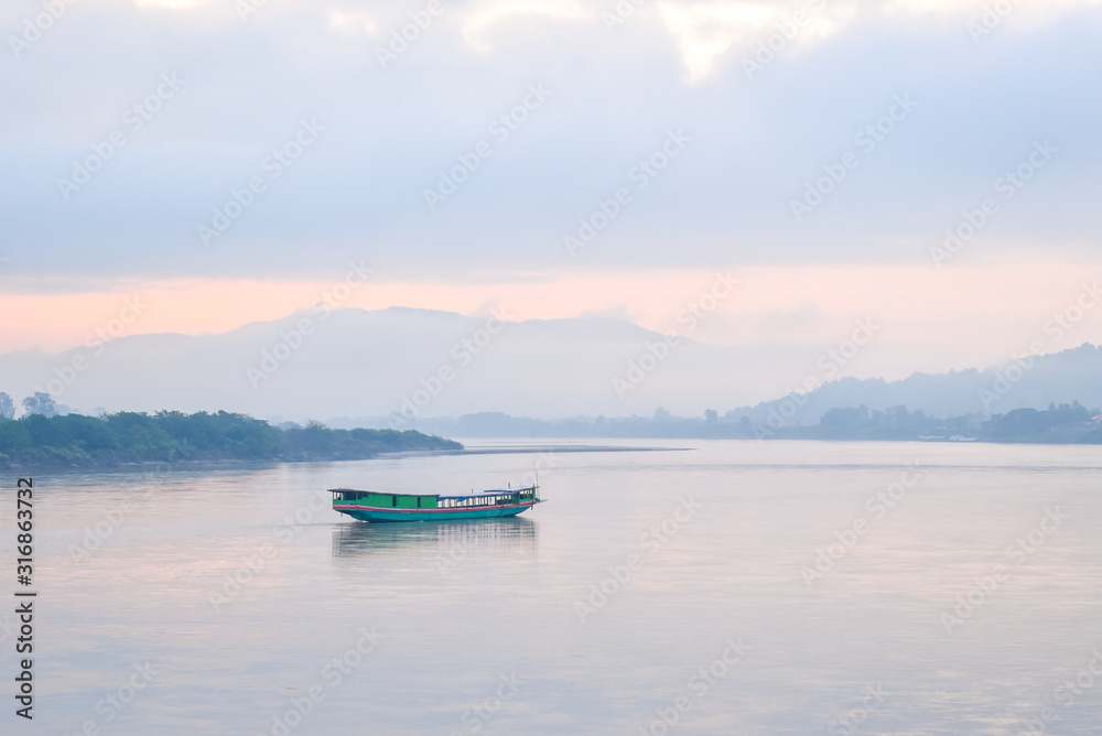 Landscape of green boat floating on the Mekong in the morning. The sky behind is cloudy and very foggy but cat see shadow of the mountains. Landscape of green boat floating on the Mekong in the morning. The sky behind is cloudy and very foggy but cat see shadow of the mountains.