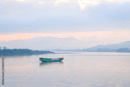 Landscape of green boat floating on the Mekong in the morning. The sky behind is cloudy and very foggy but cat see shadow of the mountains.