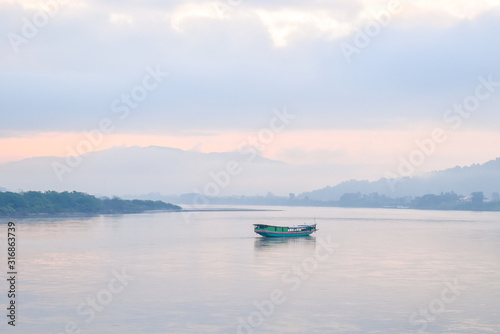 Landscape of green boat floating on the Mekong in the morning. The sky behind is cloudy and very foggy but cat see shadow of the mountains.