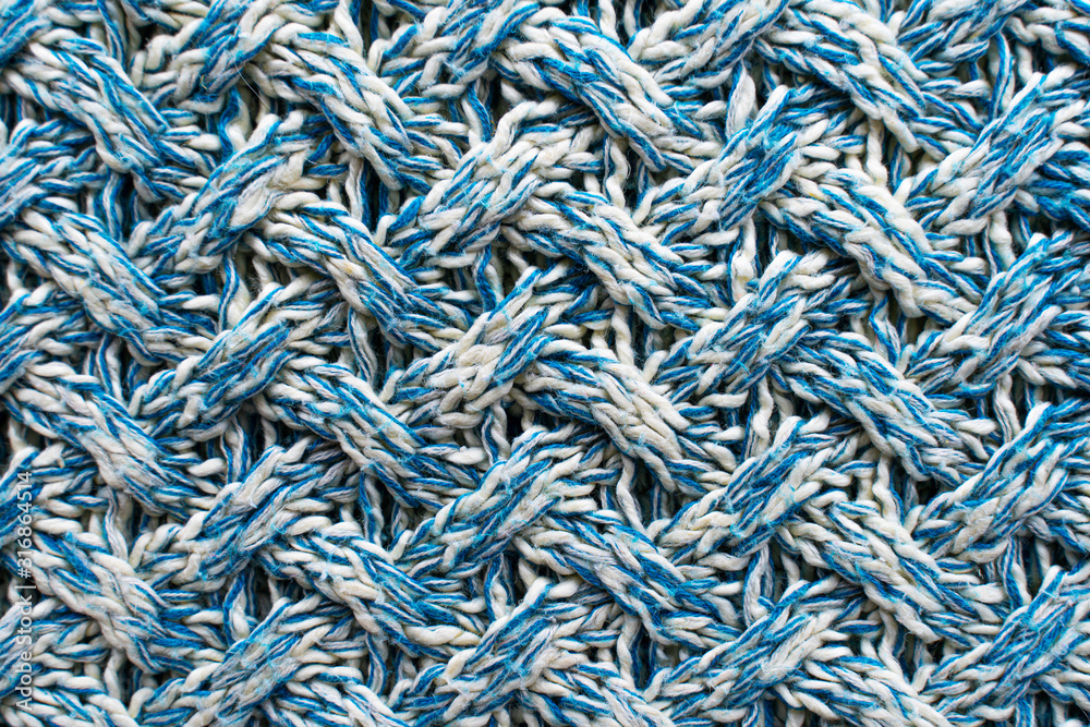 Blue and white texture of a knitted woolen fabric with a patterned weave. Sweater background
