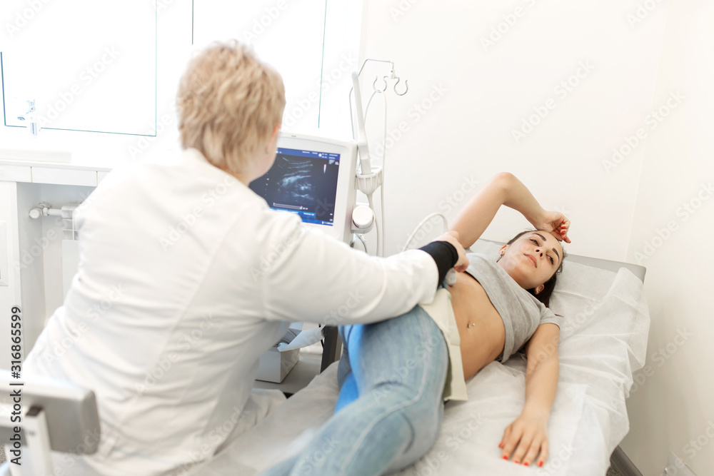 The doctor conducts an ultrasound diagnosis of the patient abdomen and internal organs. A girl lies on a couch in an ultrasound diagnostic room The doctor conducts an ultrasound diagnosis of the patient abdomen and internal organs. A girl lies on a couch in an ultrasound diagnostic room