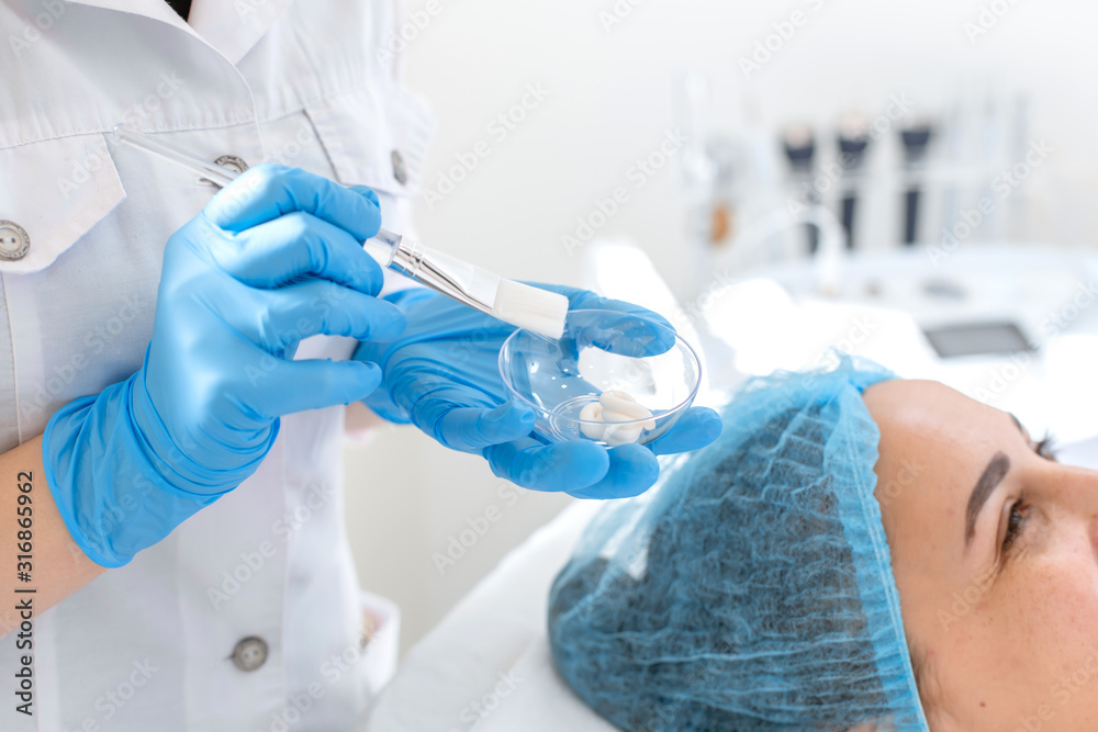 Fototapeta premium Woman professional doctor beautician prepares a mask in a glass bowl before applying the mask for skin care.