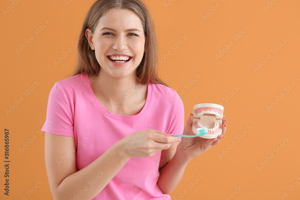 Beautiful young woman with model of jaw on color background