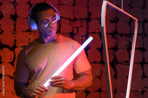 Toned portrait of African-American man with headphones and neon lamp on dark color background