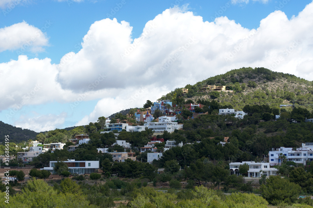 Cloudy rocky mountain with grass, trees and houses. Ibiza island, Spain