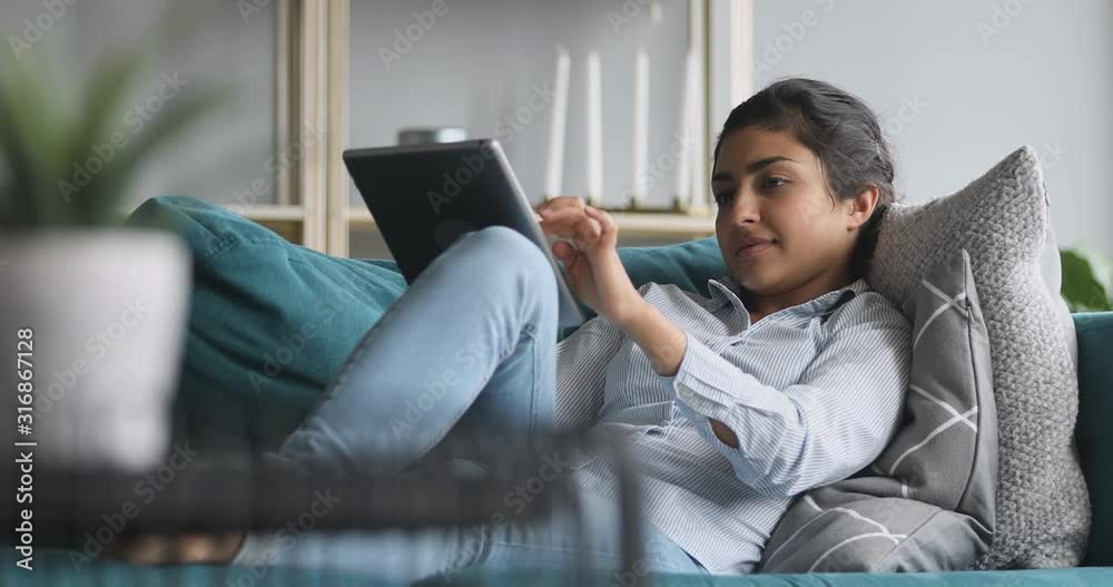 Happy indian woman relaxing on sofa holding using digital tablet Happy indian woman relaxing on sofa holding using digital tablet