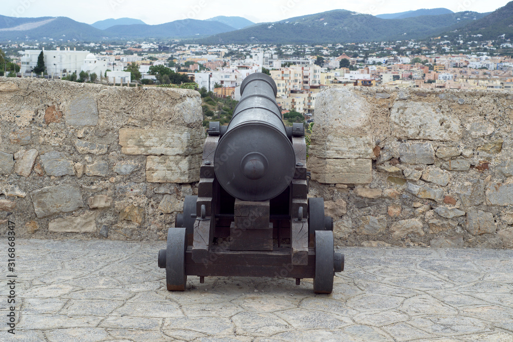 Cannon in Ibiza castle, brick walls, city and mountain view. Spain