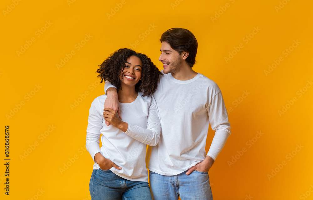 Happy multiracial couple hugging and posing together over yellow background Happy multiracial couple hugging and posing together over yellow background