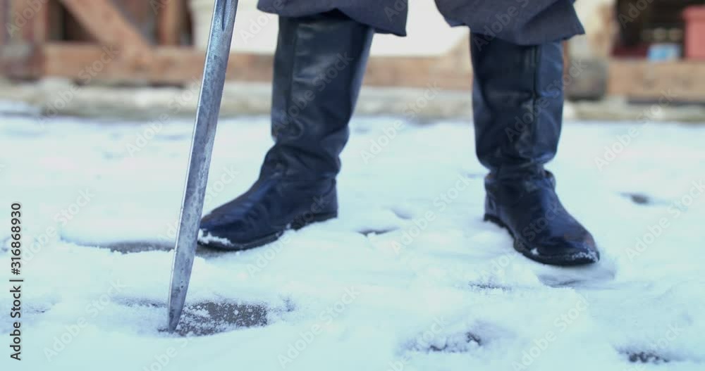 Low view of unrecognizable warrior in armor and boots hits the sword into snow