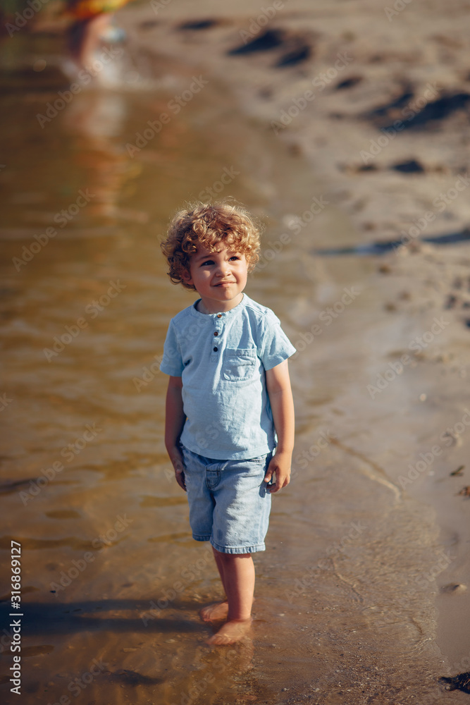 Beautiful little boy in a blue shirt. Childred playing in a summer beach. On a sand Beautiful little boy in a blue shirt. Childred playing in a summer beach. On a sand