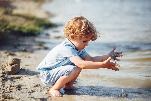 Beautiful little boy in a blue shirt. Childred playing in a summer beach. On a sand photo