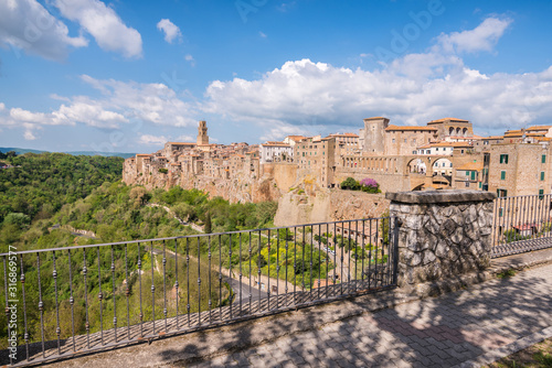 Panoramic view of Pitigliano small vilage in Italy with red brick houses and towers and nature at golden hour with beautiful sky clouds and fence in Grosseto province in Tuscany Italy photo