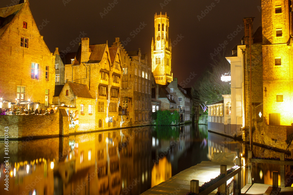 Picturesque night views to the channels and narrow streets of old Brugge in Belgium. Houses, boates, lights reflecting in the dark still water on the Christmas time.