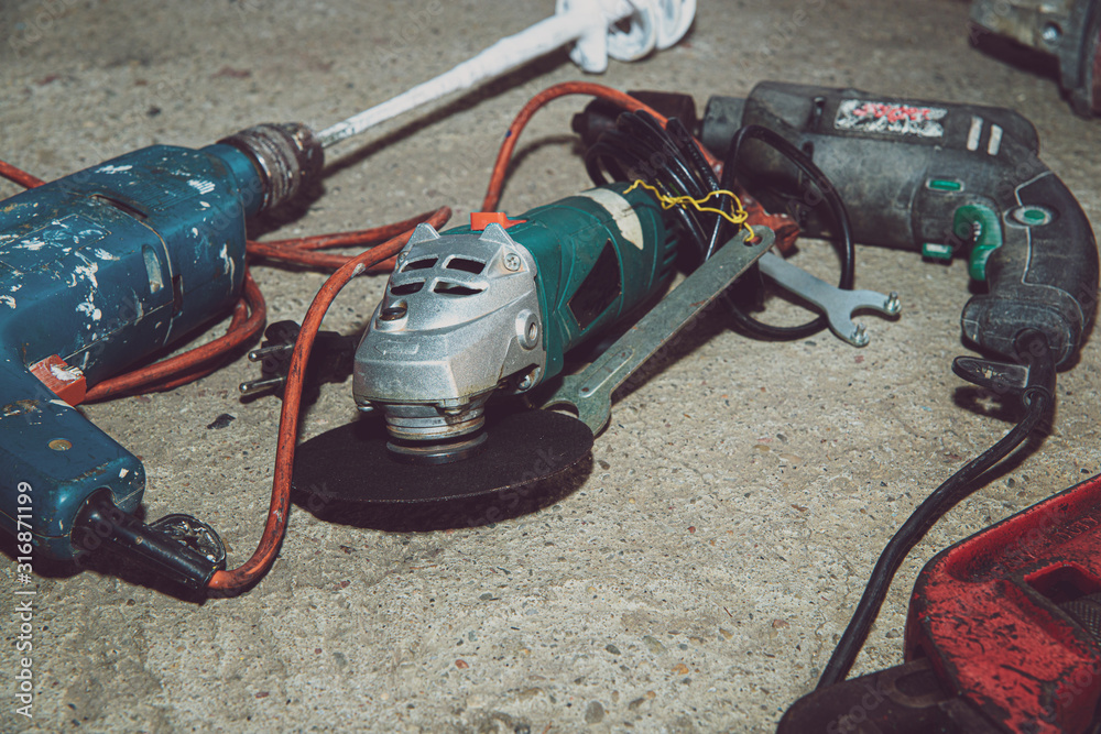 A set of power tools and tools on concrete ground. The concept of industrial work, renovation, physical work. On the ground lies a screwdriver, grinder, wrench. A set of power tools and tools on concrete ground. The concept of industrial work, renovation, physical work. On the ground lies a screwdriver, grinder, wrench.