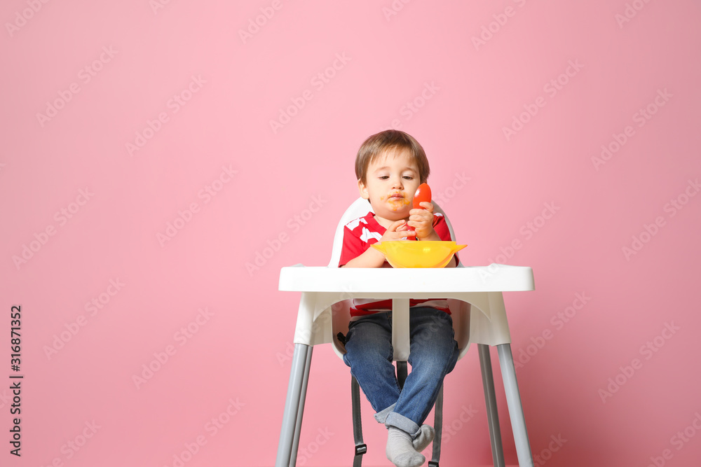 Cute little boy eating tasty baby food against color background Cute little boy eating tasty baby food against color background