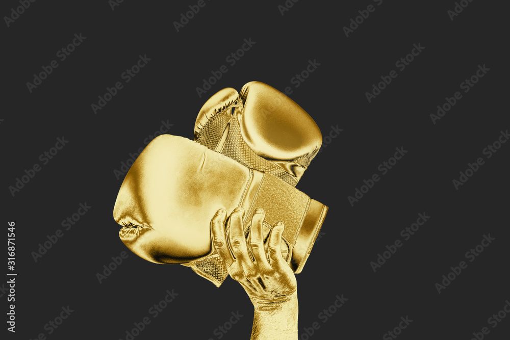 Gold boxing gloves raised up against a dark background. Victory concept