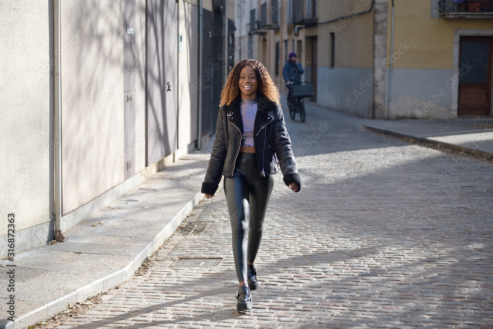 A happy black afro girl with curly brown hair walks on the street smiling A happy black afro girl with curly brown hair walks on the street smiling