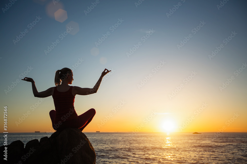 Silhouette of yoga woman on the seashore during sunset.