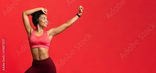 Joyful sporty girl with headset dancing over red background
