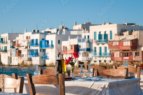 Bright scenic afternoon view of empty table waiting for sunset diners set up along the harbor in the old town of Mykonos, Greece