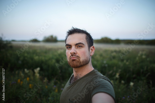 Handsome man takes a summer selfie in the middle of the meadow grass.