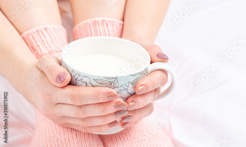 Female hands envelop a cup on a sofa early in the morning