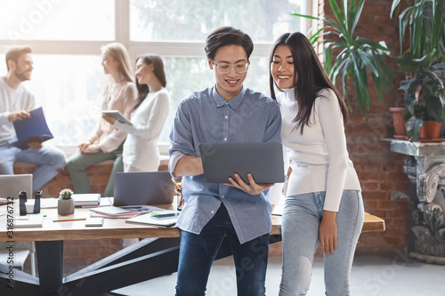 Excited asian guy sharing business ideas with young woman coworker photo