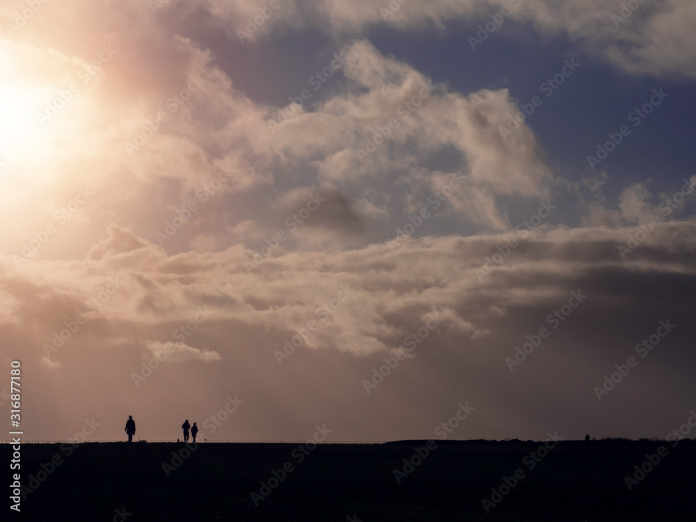 Silhouette of three people against beautiful warm cloudy sky with sun rays and flare.