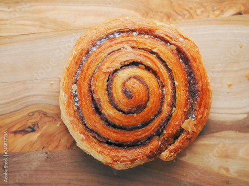 Fresh crispy cinnamon roll on a wooden board. Close up. Warm colors. Top view.