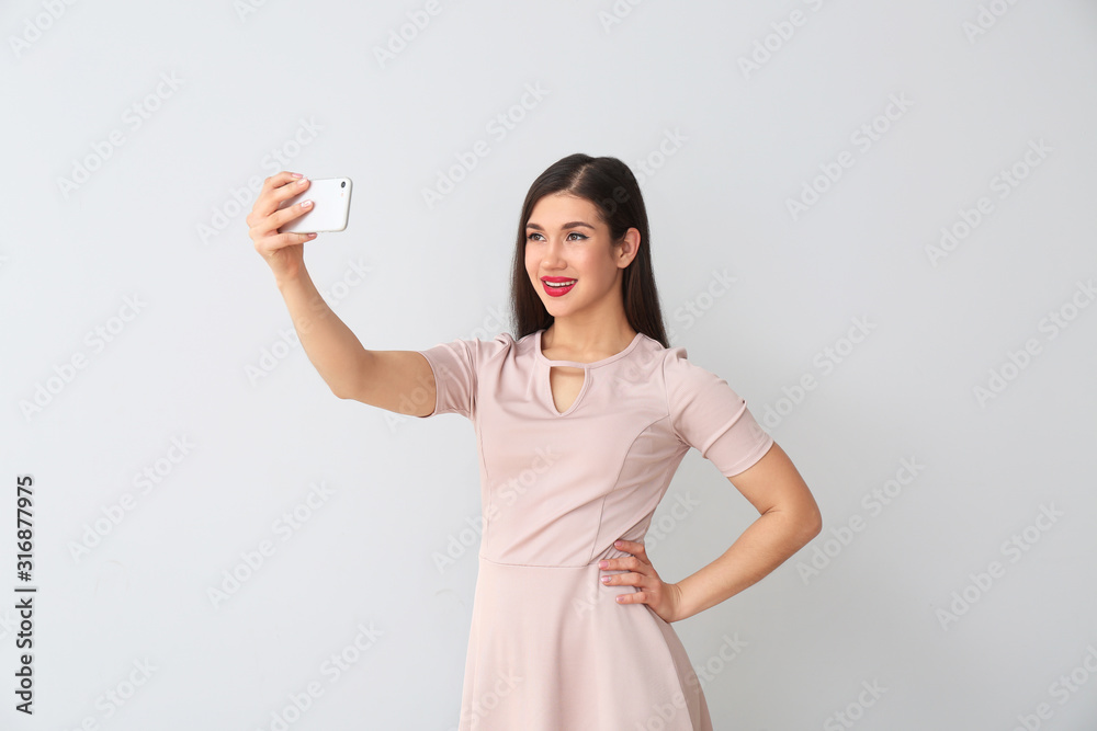 Beautiful young woman taking selfie on light background Beautiful young woman taking selfie on light background
