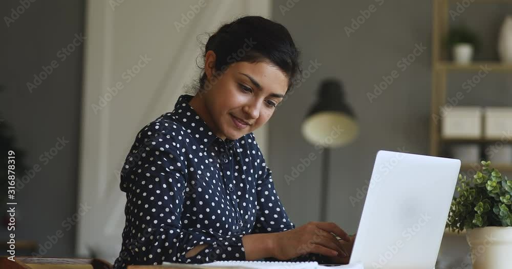 Smiling indian girl student typing on laptop preparing course work